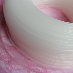 Puede incluir: Primer plano de una bobina de hilo de pl&aacute;stico blanco. La bobina est&aacute; enrollada apretadamente y tiene un acabado liso y brillante.