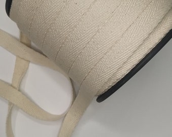 May include: A spool of natural white cotton twill tape. The tape is woven with a herringbone pattern and is wound around a black plastic spool.