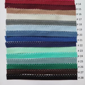 May include: A collection of 15 different colors of elastic trim with scalloped edges. The trim is arranged in rows, with each row numbered from 14 to 28.