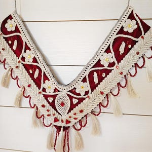 Puede incluir: Una pieza decorativa de crochet roja y blanca con borlas. La pieza tiene forma de V y tiene una franja de cuentas.