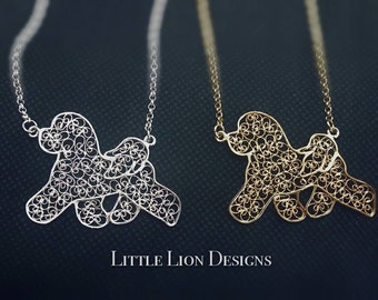 Puede incluir: Dos collares de plata y oro con un diseño de filigrana de un perro. Los collares cuelgan sobre un fondo oscuro. El texto "LITTLE LION DESIGNS" está en la parte inferior de la imagen.