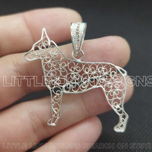 Può includere: Ciondolo in filigrana d'argento a forma di cane. Il ciondolo è dettagliato e intricato, con un design delicato. Il ciondolo è appeso a una catena d'argento.