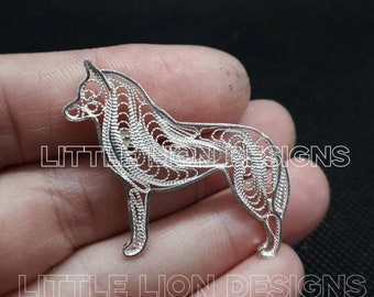 Op de afbeelding: Een zilveren filigraan hanger in de vorm van een hond. De hanger is gedetailleerd en ingewikkeld, met een delicaat ontwerp. De hanger wordt in een hand gehouden, met de woorden "LITTLE LION DESIGNS" zichtbaar op de achtergrond.