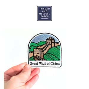 Könnte beinhalten: Gestickter Aufnäher mit der Großen Mauer Chinas. Der Aufnäher zeigt einen hellblauen Himmel, grüne Hügel und eine beige Mauer. Der Text "Great Wall of China" steht unten. Der Aufnäher wird von einer Hand gehalten.
