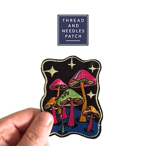 Può includere: Toppa ricamata con funghi colorati con cappelli rosa, verdi e arancioni su sfondo nero stellato. La toppa ha un bordo dorato e il testo "THREAD AND NEEDLES PATCH" in un quadrato blu navy.