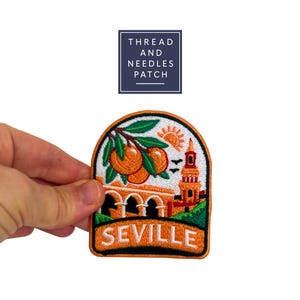 May include: Embroidered patch featuring a Seville, Spain design. The patch includes a depiction of oranges, a bridge, a tower, and the word "SEVILLE". The patch is orange, green, and white with black borders. The text "THREAD AND NEEDLES PATCH" is above the patch.