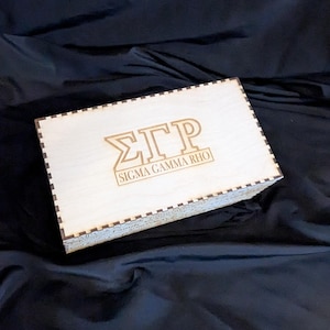 May include: A wooden box with a black and white checkered border. The box is engraved with the letters "ΣΓΡ" and the words "Sigma Gamma Rho".