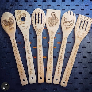 May include: Six wooden spoons with chicken designs and humorous sayings. The sayings include "Don't like dinner? Find the eggs", "Feelin Peckish? Here's an egg", "Heyley It's the Crazy Chicken Lady!", "Cooking around the cluck!", "Made from scratch! 1-gg-cellent!" and "Burned? Zero Glucks Given."