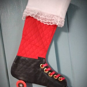 May include: A Christmas stocking shaped like a roller skate. The stocking features a red quilted body, black skate, and white cuff with lace trim. Gold eyelets and red laces add detail. Orange wheels complete the design.