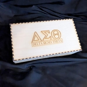 May include: A wooden box with a black and white checkered border. The box is engraved with the letters "ΔΣΘ" and the words "Delta Sigma Theta".