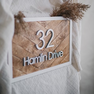 May include: A white framed wooden sign with a herringbone pattern. The sign has the number 32 and the text "Hamlin Drive" in white raised letters.