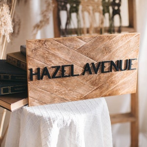 May include: Wooden sign with a chevron pattern and the text "HAZEL AVENUE" in black letters.