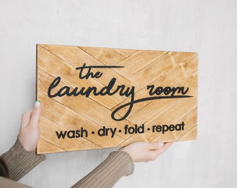 May include: A wooden sign with a chevron pattern reads "the laundry room wash - dry - fold - repeat".