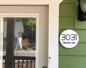 May include: White round house number sign with black numbers and text. The sign reads "3031 Clemson Ave".