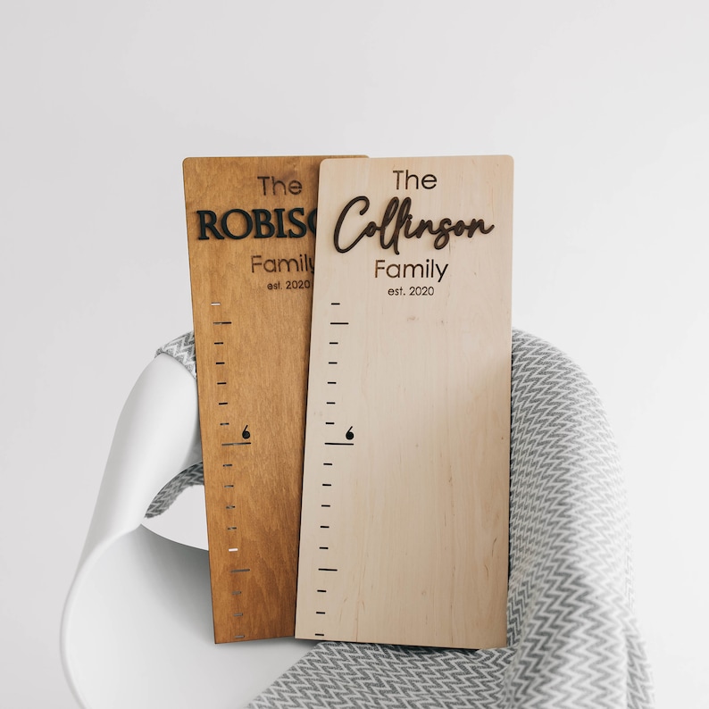 Puede incluir: Dos tablas de crecimiento de madera con una regla y el texto "The Robinson Family est. 2020" y "The Collinson Family est. 2020".