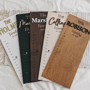 Puede incluir: Seis tablas de crecimiento de madera con diferentes nombres de familia y fechas de establecimiento. Las tablas est&aacute;n en varios tonos de madera, incluyendo blanco, negro, marr&oacute;n y madera natural. Cada tabla tiene una regla marcada en pulgadas.