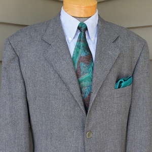May include: A gray blazer with a patterned tie and a green pocket square.