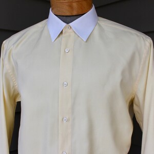May include: A pale yellow long-sleeved dress shirt with a white collar and button-up front.