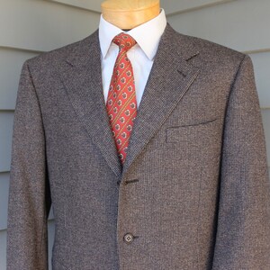 May include: A brown and black patterned blazer with a single button closure. The blazer has a red patterned tie.