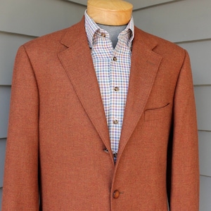 May include: A rust-colored blazer with a single button closure. The blazer has a classic fit and a smooth texture.