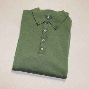 May include: A green long-sleeved knitted polo shirt with a button-up collar and gold buttons. The shirt is folded and laid flat on a light beige surface.