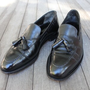 May include: A pair of black leather tassel loafers with a polished finish. The loafers have a pointed toe and a low heel.