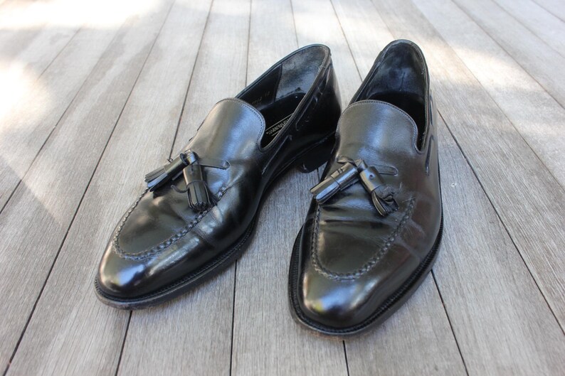 May include: A pair of black leather tassel loafers with a polished finish. The loafers have a pointed toe and a low heel.