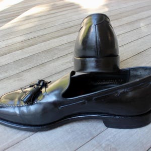May include: A pair of black leather tassel loafers. One loafer is lying on its side, while the other is standing upright.