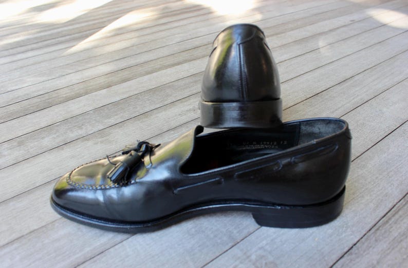 May include: A pair of black leather tassel loafers. One loafer is lying on its side, while the other is standing upright.