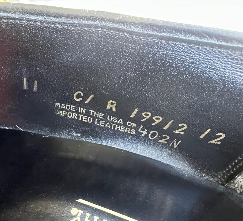 May include: Close-up of a black leather shoe sole with the text "C/R 19912 12 MADE IN THE USA OF IMPORTED LEATHERS 402N"
