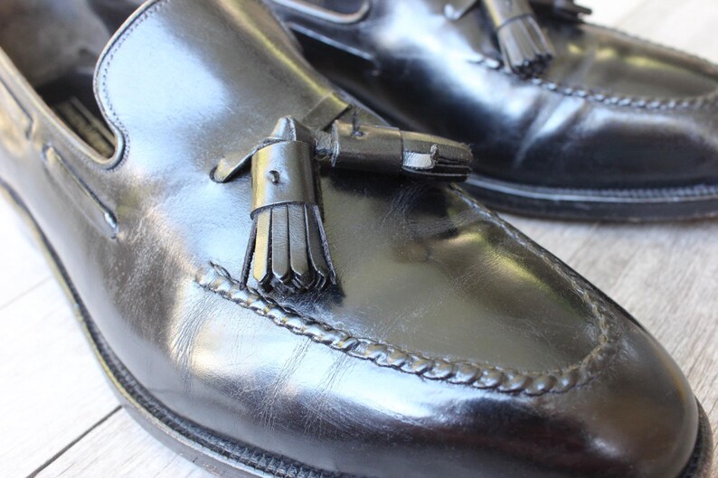 May include: A pair of black leather tassel loafers with a braided trim around the toe. The loafers have a classic design and are made of high-quality leather.
