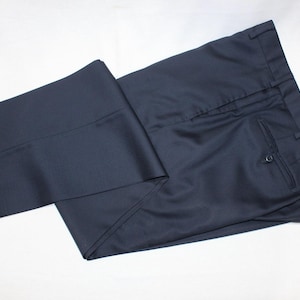 May include: A pair of dark blue dress pants folded in half. The pants have a single pleat on the front and a back pocket with a button.