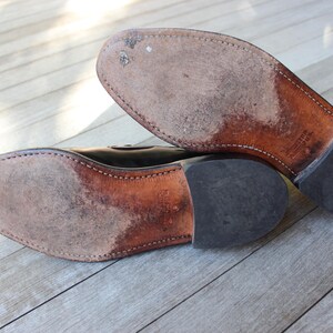May include: Close-up of the soles of a pair of black leather shoes. The shoes have a brown leather sole and a black rubber heel.