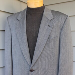 May include: A gray blazer with a subtle herringbone pattern. The blazer has a single button closure and a pocket on the left side.