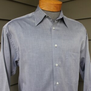 May include: A light blue long-sleeved button-down shirt with a pocket on the left side.
