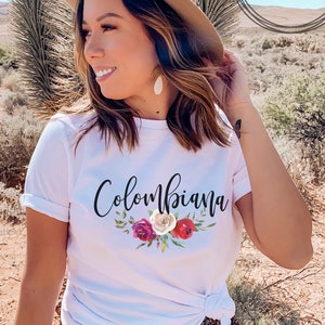 May include: White t-shirt with the text "Colombiana" in black script with a floral design in red, white, and pink.