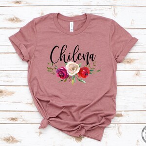 May include: A mauve t-shirt with the word "Chilena" in black script and a floral design featuring red, white, and pink roses.