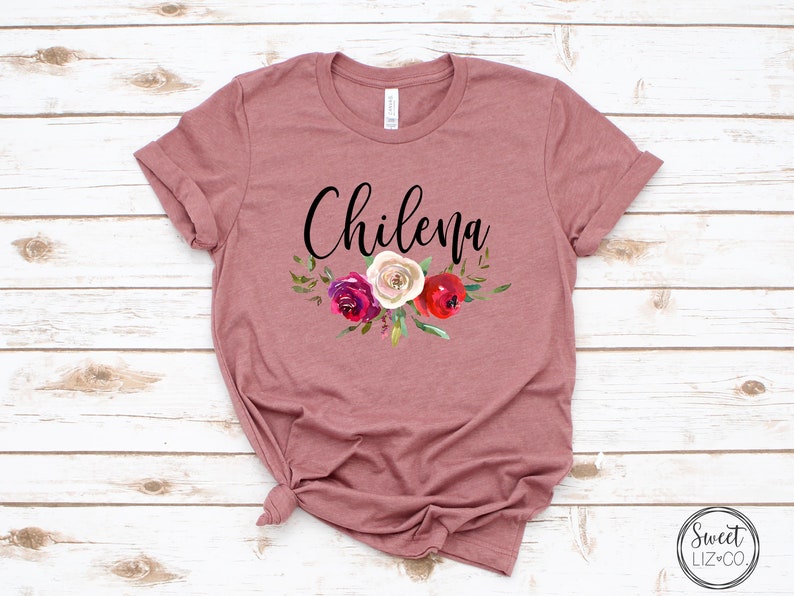 May include: A mauve t-shirt with the word "Chilena" in black script and a floral design featuring red, white, and pink roses.