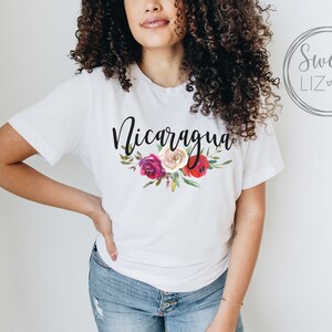 May include: White t-shirt with the word "Nicaragua" in black script and a floral design with red, pink, and white flowers.