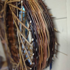 May include: A woven wreath made of brown and tan twigs, with a circular shape and a slightly uneven texture.