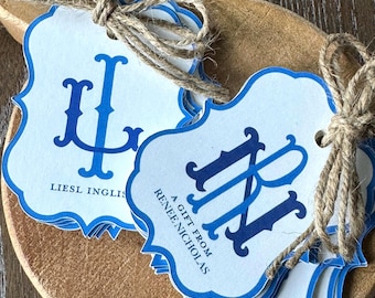 May include: A stack of white scalloped gift tags with blue borders and blue monogram lettering. One tag features the text LIESL INGLIS and the other reads A GIFT FROM RENEE NICHOLAS. Each tag is tied with a brown jute twine bow for attachment.