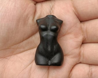 Pode incluir: Pequena figura negra esculpida de um torso feminino. A escultura é lisa e polida, com curvas e detalhes definidos. A figura é segurada em uma mão, mostrando seu tamanho e forma.