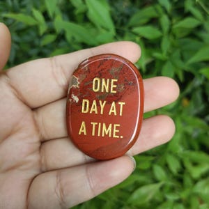 May include: Red stone with the words "ONE DAY AT A TIME" written in gold lettering.