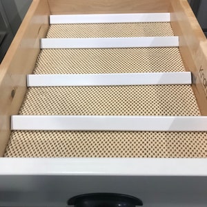 May include: A white drawer liner with four white dividers. The liner is made of a textured material and is designed to keep items organised in a drawer.