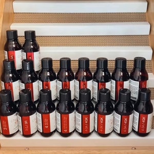 May include: A collection of small, clear glass bottles with brown liquid inside. The bottles are arranged in rows on a wooden shelf. Each bottle has a white label with black text indicating the product's name and size. The labels read "3", "3-5/3R", "4", "4", "4-34/4GK", "4-34/4GK", "4-34/4GK", "4-34/4GK".