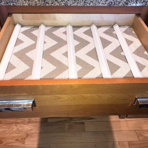 May include: A wooden drawer with a white and gray chevron patterned liner and white dividers. The drawer has two silver handles.
