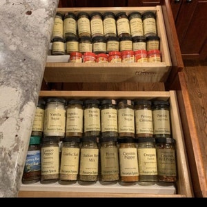 May include: A drawer filled with small glass jars of spices, labeled with the names of the spices, such as "Vanilla Sugar", "Paprika", "French Thyme", "Garlic Salt", "Italian Herb Mix", "Pizza Seasoning", "Cayenne Pepper", "Oregano", and "Crushed Red Pepper".