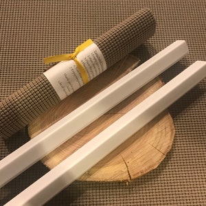 May include: Two white wooden dowels with hexagonal ends, lying on a wooden slice. A rolled-up brown yoga mat with a yellow ribbon and a handwritten note is in the background.