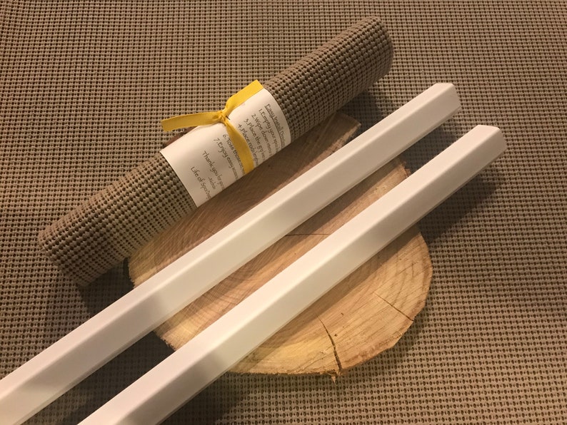 May include: Two white wooden dowels with hexagonal ends, lying on a wooden slice. A rolled-up brown yoga mat with a yellow ribbon and a handwritten note is in the background.