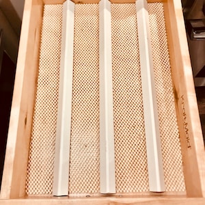 May include: Three white plastic drawer dividers in a wooden drawer with a beige patterned liner. The drawer liner is labeled "KraftMaid".